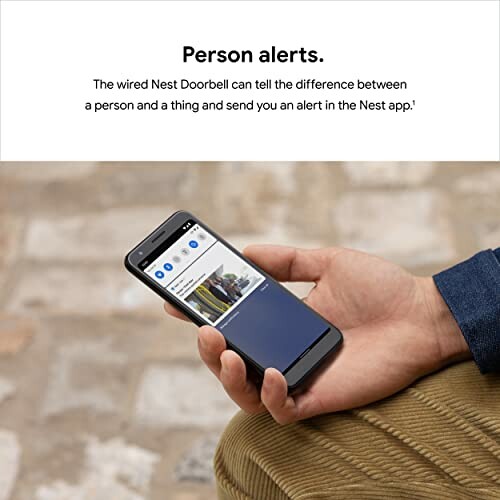 Hand holding phone showing Nest Doorbell alert with text about person alerts.
